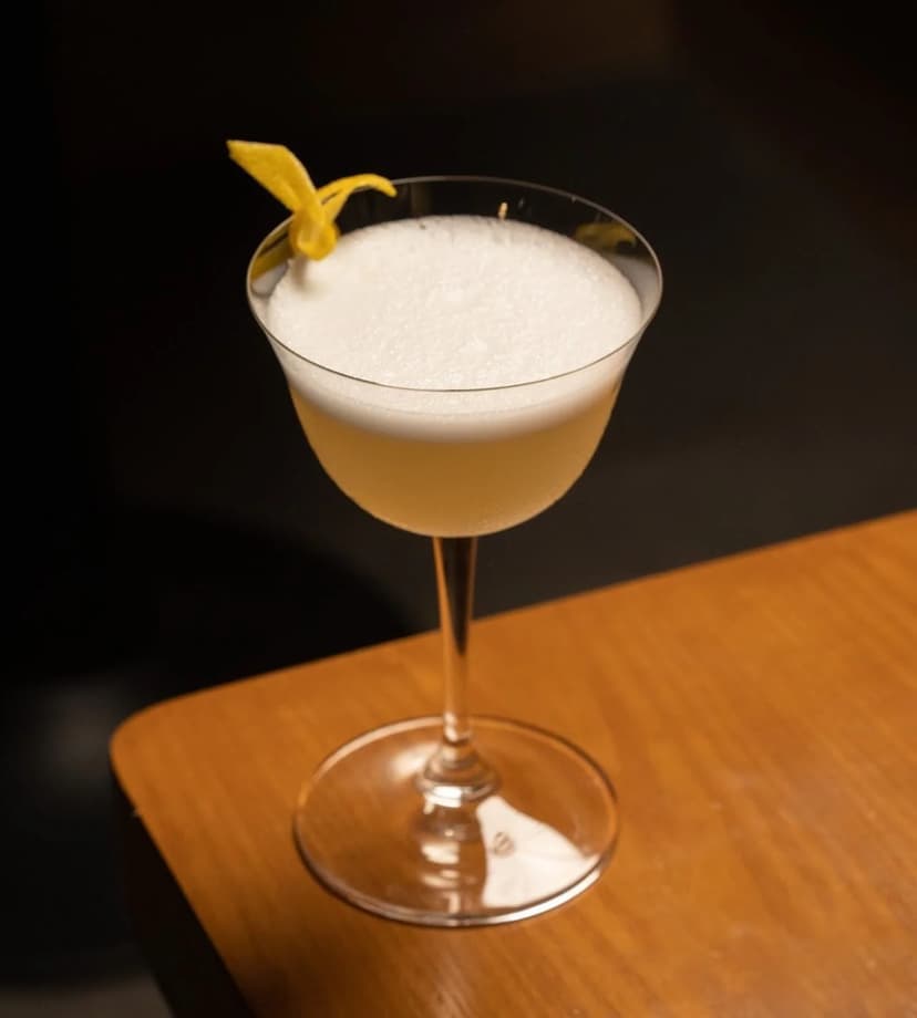 A craft cocktail served in a coupe with a lemon twist and a fine foam, resting on the bar at Bar Filo
