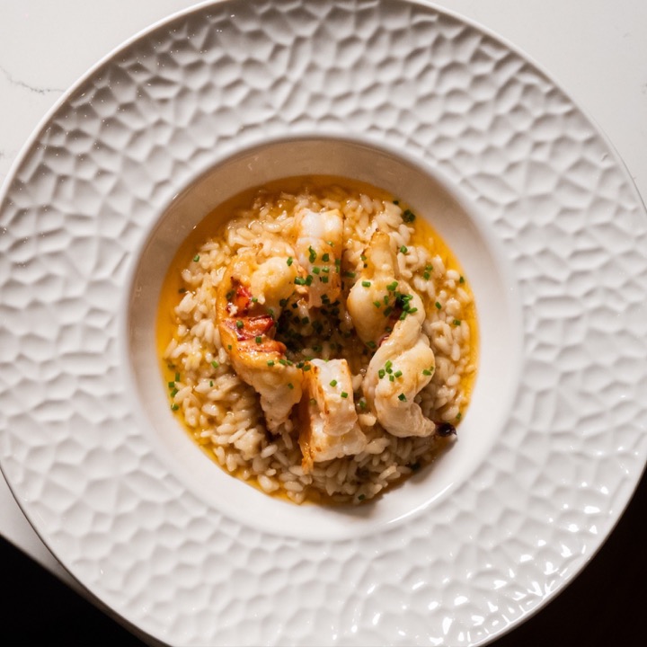 Creamy risotto topped with a whole lobster tail, tiger shrimp and fresh chives on hammered white porcelain